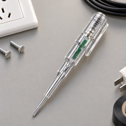 A clear electrical tester screwdriver with a flat head tip rests on a gray surface with screws and electrical tape.