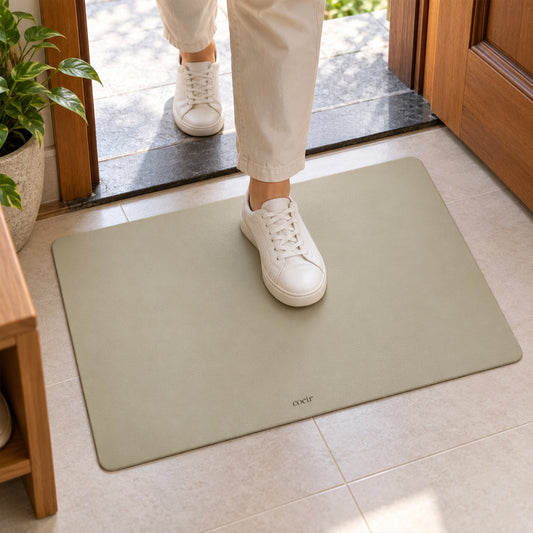 A person in white sneakers steps onto a light beige rectangular floor mat by a doorway.