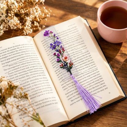 A transparent bookmark with a purple floral design and a matching tassel marks a page in an open book.
