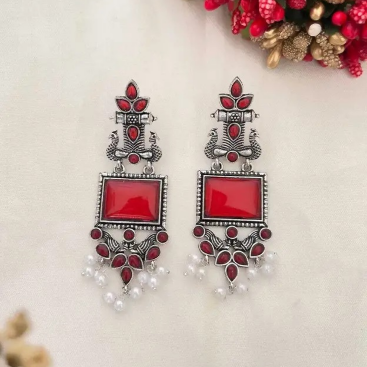 Side angle of oxidized silver traditional earrings with red stones and dangling pearl drops