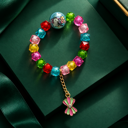 A multicolored beaded bracelet with a light blue Hello Kitty bead and a pink bow charm on a dark green background.
