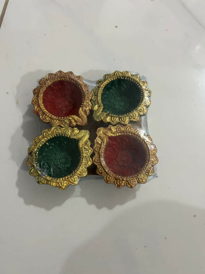 Four red and green clay diyas with gold accents, individually wrapped in plastic on a white tiled floor.