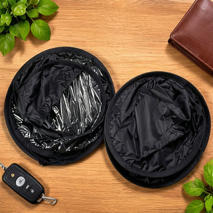 Two black circular folded car sunshades on a wooden table, next to car keys and a brown wallet.