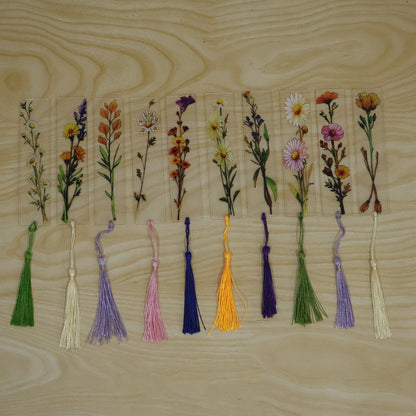 Transparent floral bookmark with a red flower and a yellow tassel, lying on a book with open pages