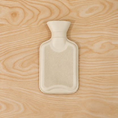 A cream hot water bottle with a ribbed surface lies flat on a light wooden table.