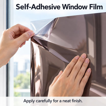 Hands carefully peeling the clear backing from a sheet of brown reflective window film against a bright window.
