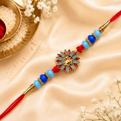 A red thread bracelet with a gold Ganesh charm, blue and light blue beads, and gold accents, on a cream satin fabric with