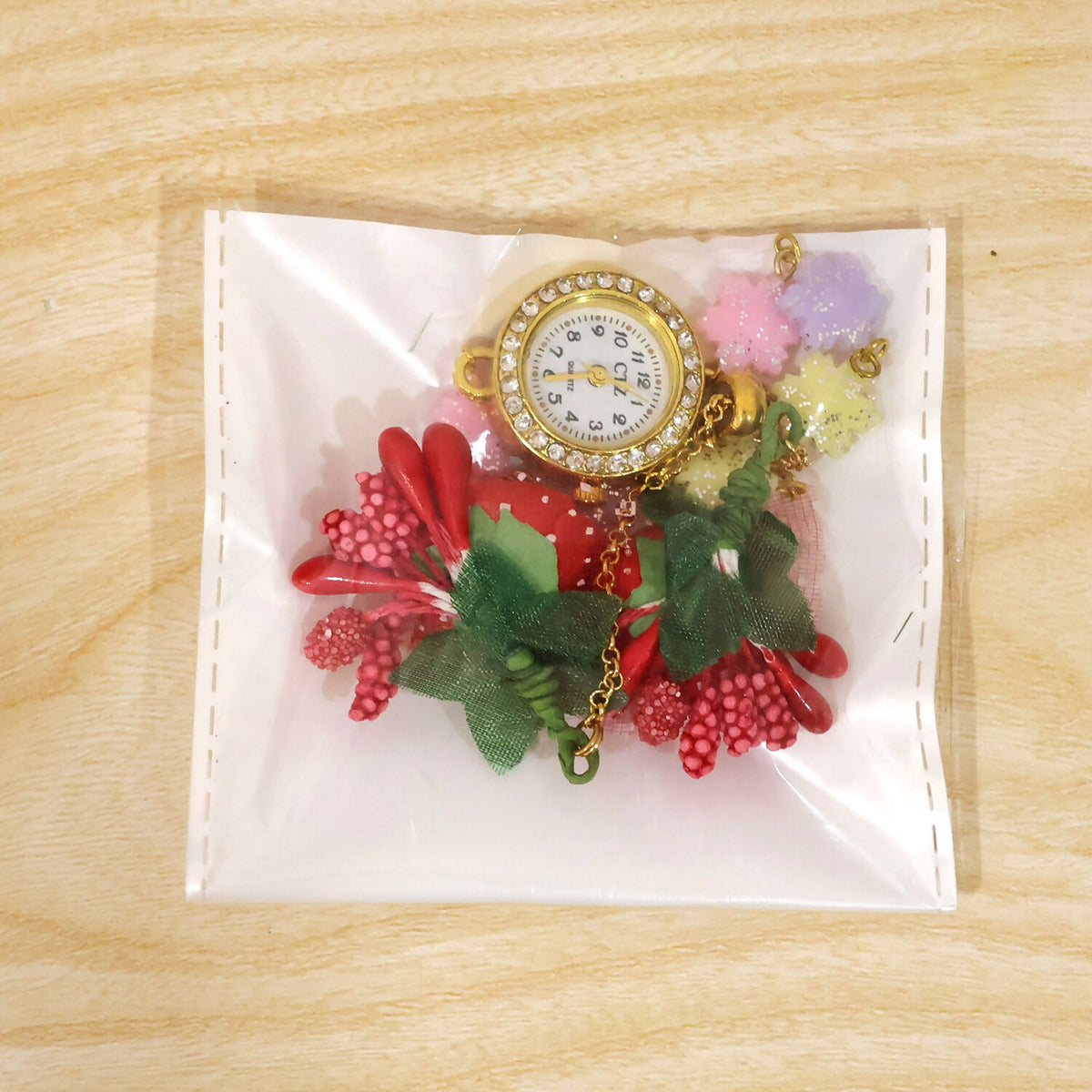 The watch and charms are packaged inside a clear plastic bag on a light wooden surface.