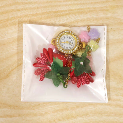 The watch and charms are packaged inside a clear plastic bag on a light wooden surface.