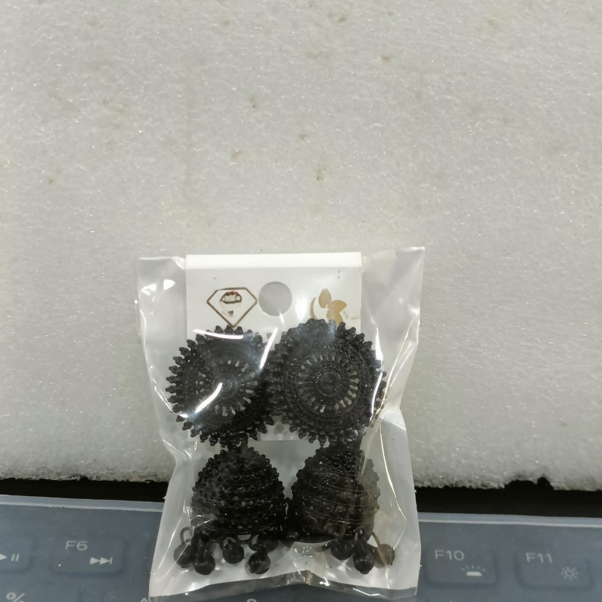 The black oxidised jhumka earrings are sealed in clear plastic packaging, ready for shipment.