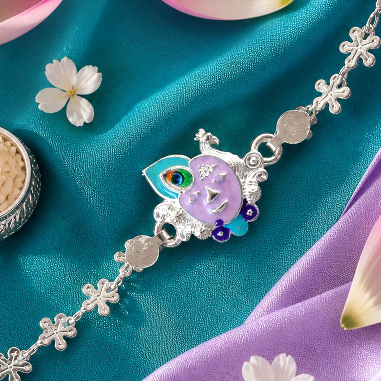 Close-up of a silver rakhi with a purple enamel Krishna face and peacock feather charm on teal and purple fabric.