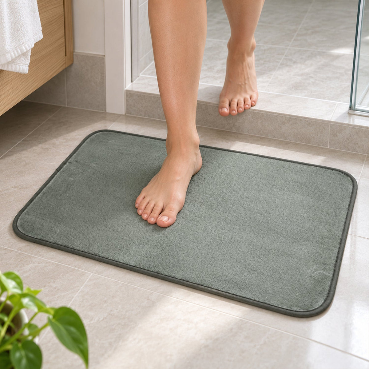 Bare feet stepping onto a gray rectangular floor mat from a tiled bathroom floor near a shower.