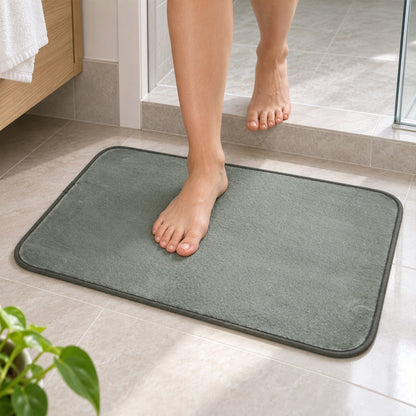 Bare feet stepping onto a gray rectangular floor mat from a tiled bathroom floor near a shower.
