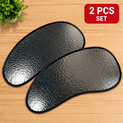 Two silver reflective car sunshades with black edges lying on a wooden surface next to a small plant.