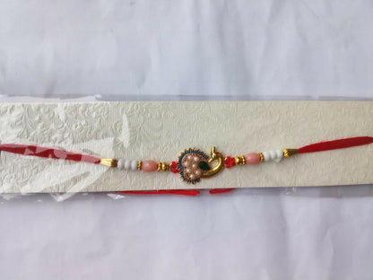 A red thread with a gold peacock charm, pink and white beads, and gold accents, displayed in clear packaging on a textured