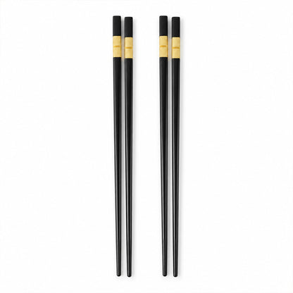 Two pairs of sleek black chopsticks with golden accents are arranged vertically on a plain white background.