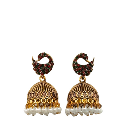 A pair of gold jhumka earrings with red and green stones and pearl drops on a white background.