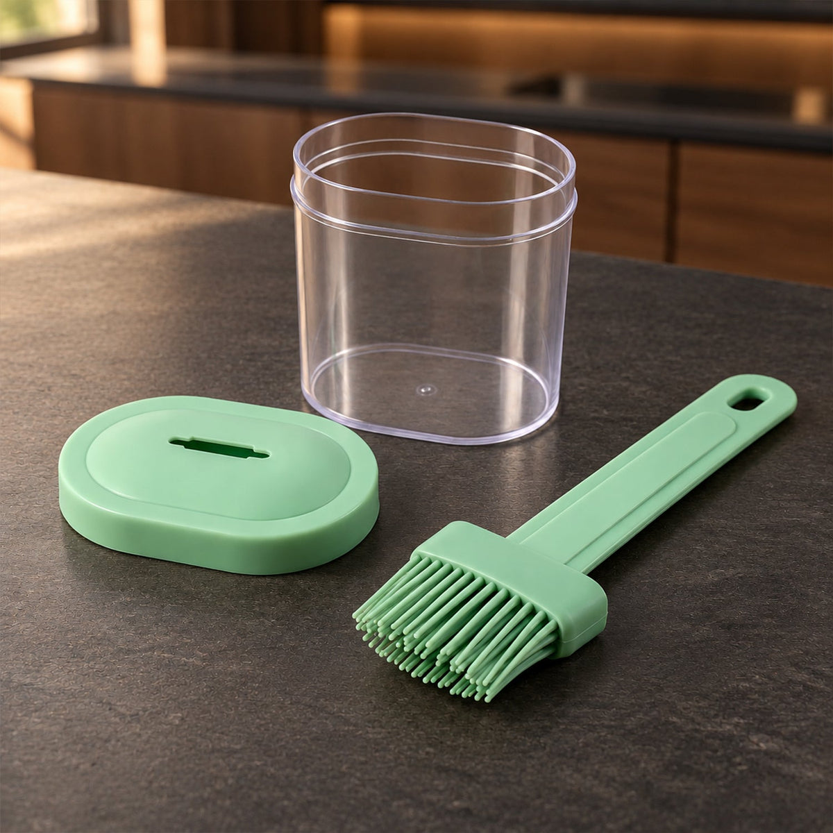 A light green silicone basting brush, a clear empty oil container, and its matching green lid are arranged on a dark