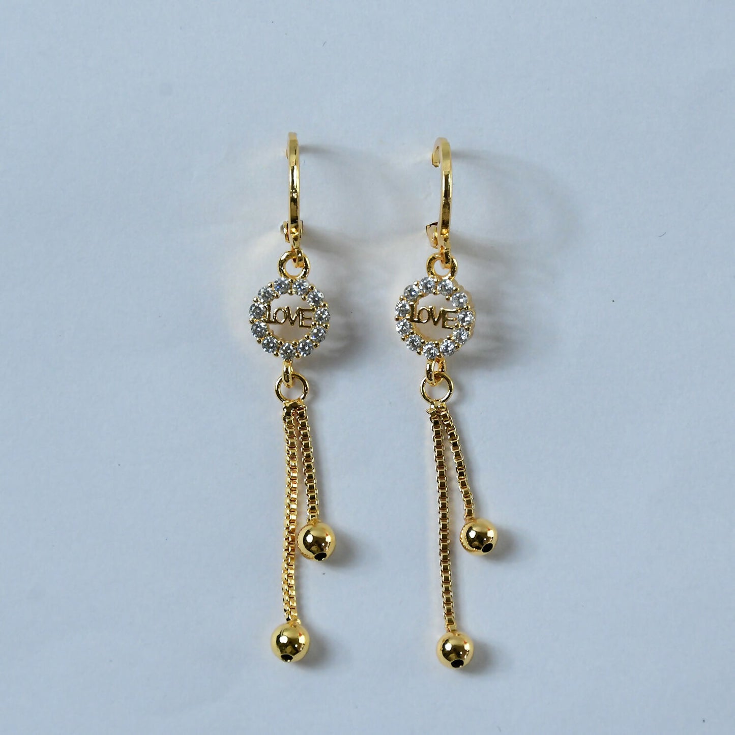 Close-up image showing crystal-encrusted “LOVE” charm in gold-finish earrings