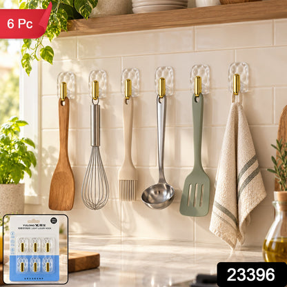 Six clear plastic hooks with gold accents hold kitchen utensils and a towel on a white tiled wall, with the product