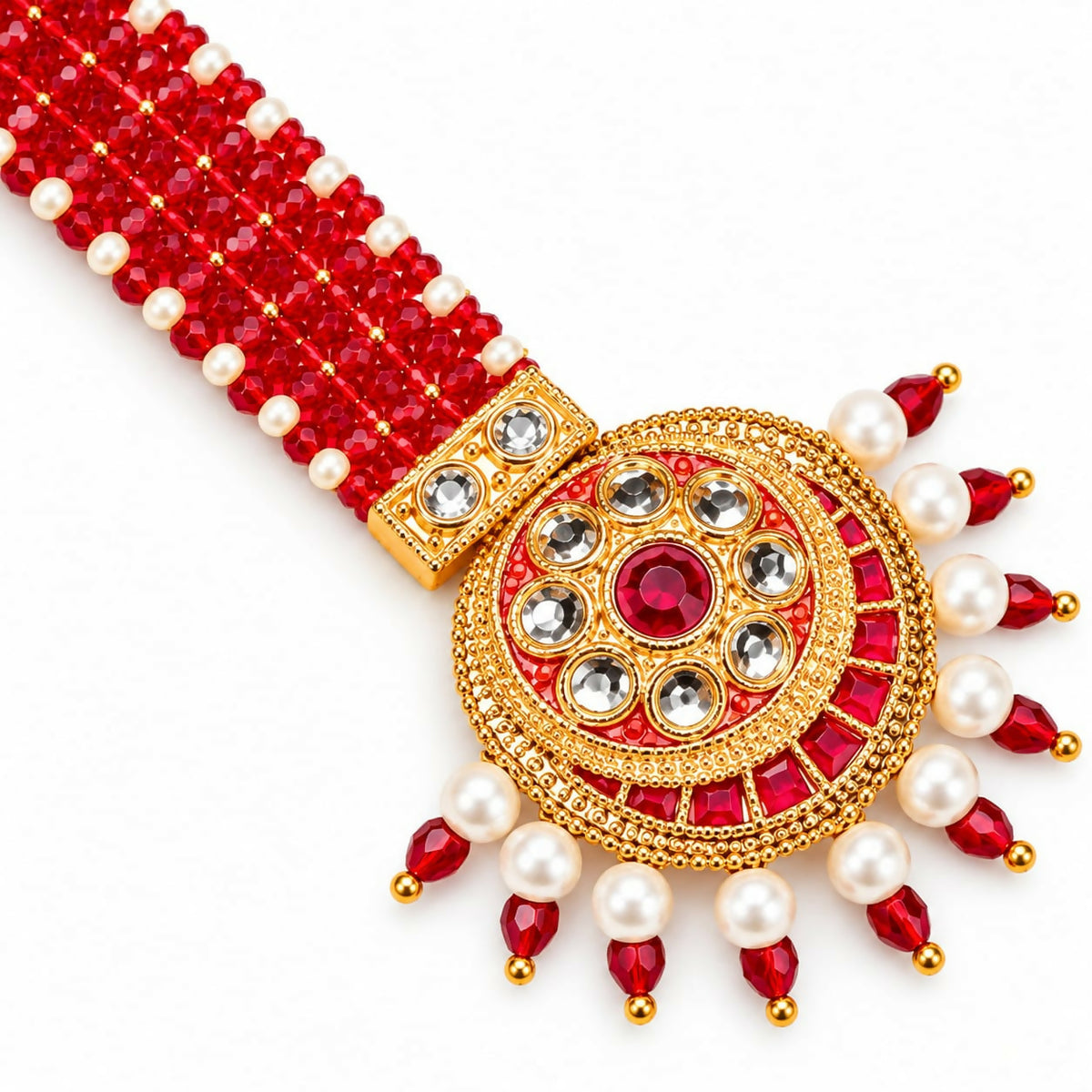 A close-up of a gold-plated maang tikka with red and white beads, featuring a circular pendant with a central red gem, on a