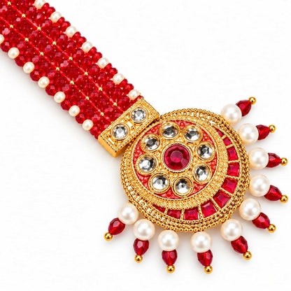 A close-up of a gold-plated maang tikka with red and white beads, featuring a circular pendant with a central red gem, on a