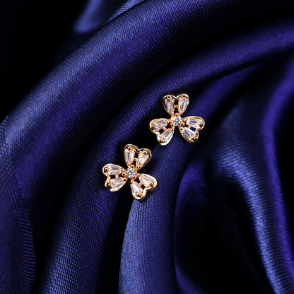 Pair of gold finish floral CZ stud earrings lying on neutral background