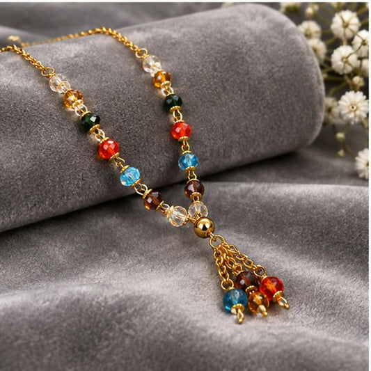 Gold chain necklace with a tassel pendant and colorful beads on a gray velvet display.