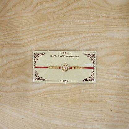A devotional thread on a decorative card, featuring a white and gold circular charm with a red and white U-shaped symbol, on