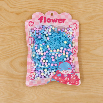 A clear bag of blue shredded paper and pastel foam balls, featuring a cartoon character, rests on a light wood surface.