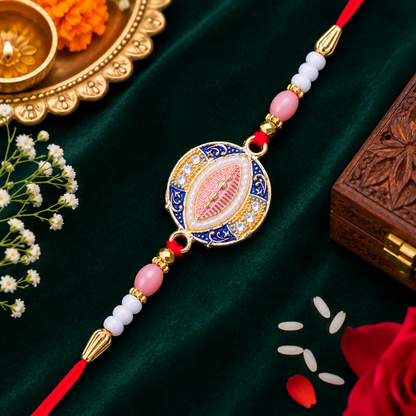 A blue, pink, and gold Rakhi with a central oval design, surrounded by small white stones and pearls, rests on a dark green