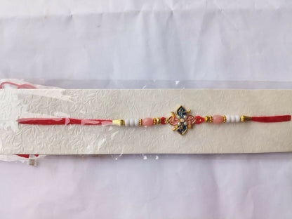 A red and white beaded bracelet with a central pink and blue floral charm is presented on a white, textured card against a