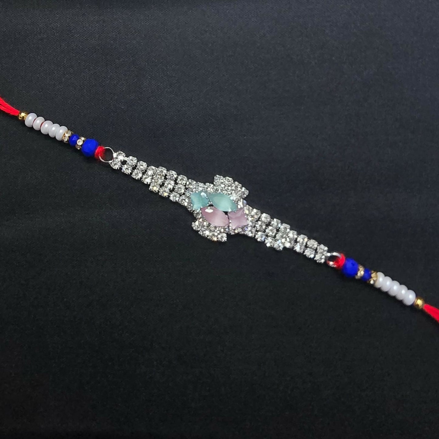 The crystal floral designer Rakhi, adorned with blue beads and red thread, is simply laid out on a plain black background.