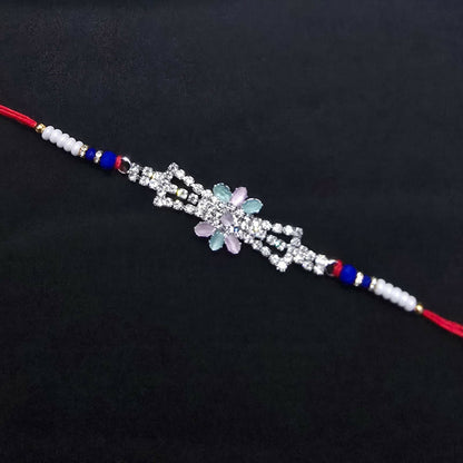 The elegant Rakhi, featuring a crystal floral design, blue beads, and red thread, is presented against a plain dark