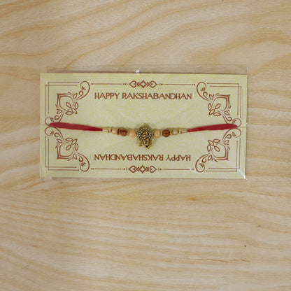 Antique Deity Idol Devotional Rakhi with Golden Medallion, Peach Beads and Red Thread