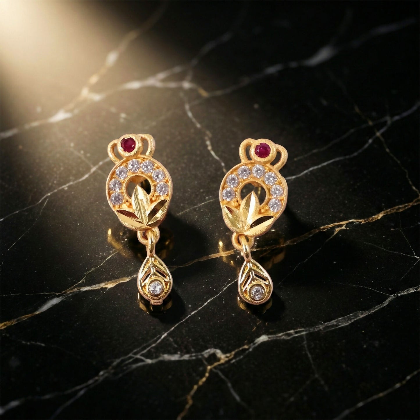 Gold floral drop earrings with ruby center and white stones on dark background