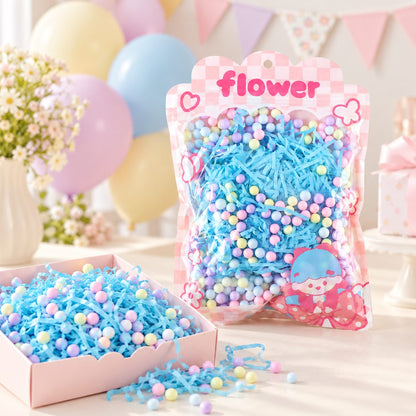 A clear bag of blue shredded paper and pastel foam balls next to an open pink box filled with the same items.
