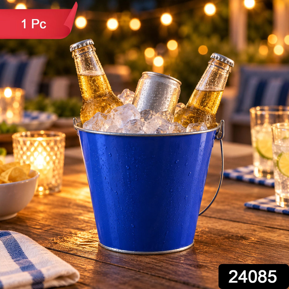 A blue metal bucket filled with ice and drinks on a wooden table at an outdoor evening party, with string lights and snacks.