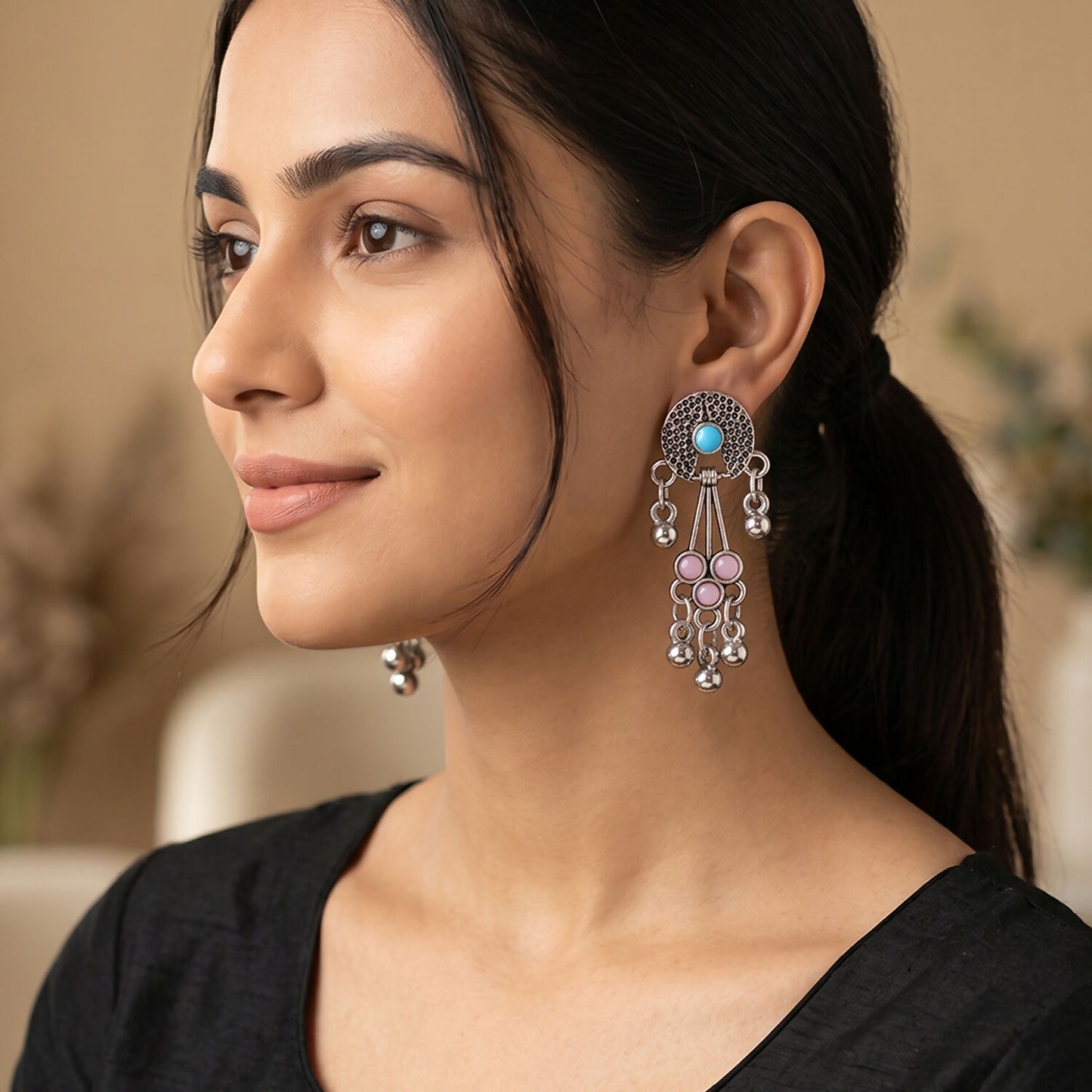 A woman models one oxidised silver long drop earring with pink and turquoise stones and ghungroo bells, looking left.