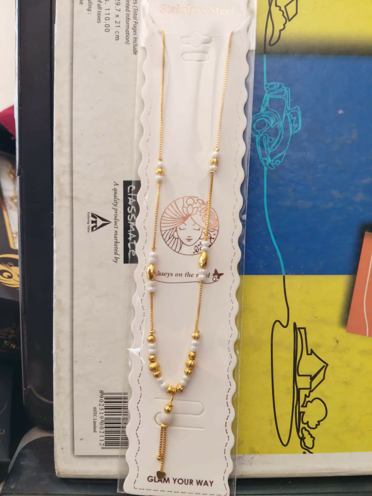 A gold tone necklace with white pearls and gold beads in its original packaging.
