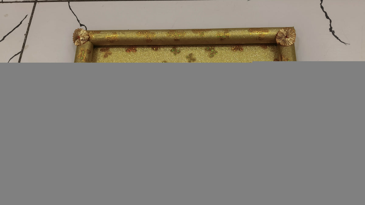 A golden rectangular tray with decorative rolled edges and a patterned surface is seen from a high angle.