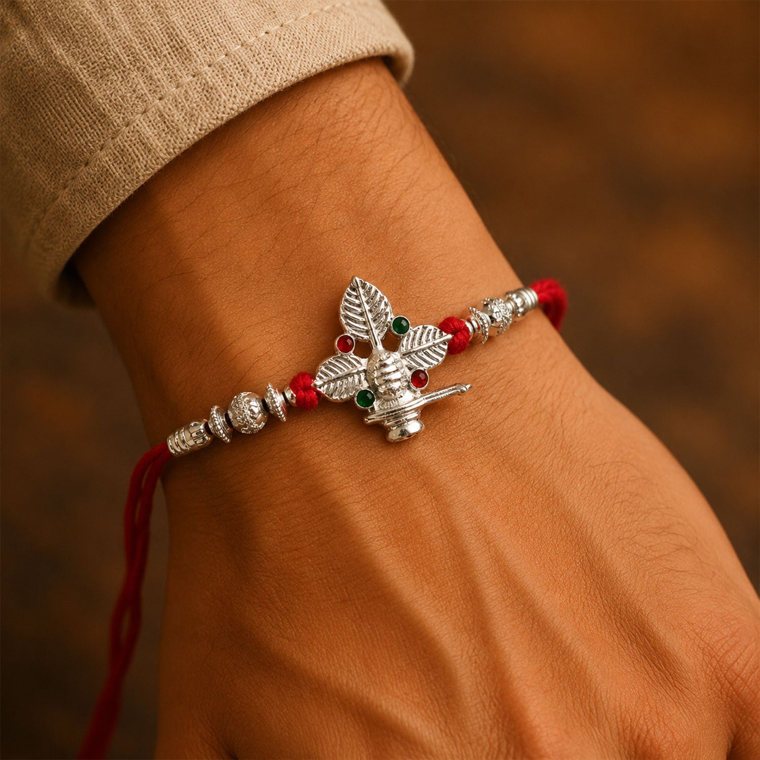 Silver Shivling Leaf Rakhi with Green Stones and Bright Red Thread