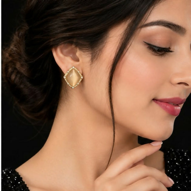 A woman models a single champagne geometric stud earring, showcasing its size and placement on her earlobe.