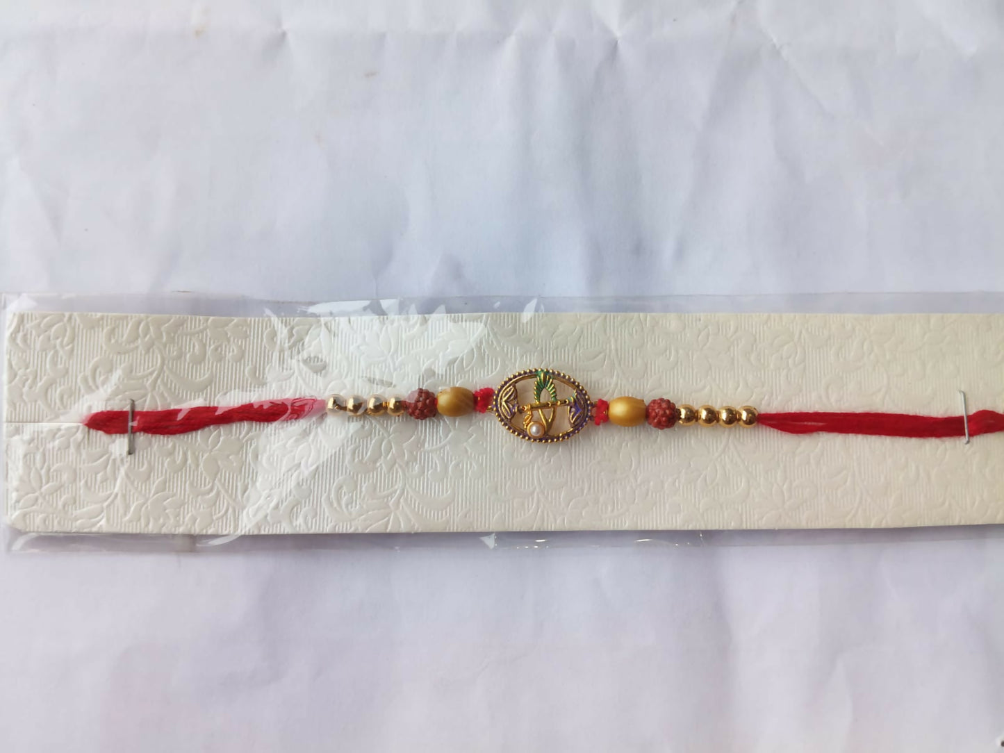 A red thread bracelet with a purple oval charm and beads is presented in clear packaging on a white textured card.