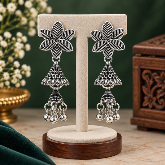 A pair of oxidised silver floral jhumka earrings with two tiers and ghungroo drops, displayed on a stand.