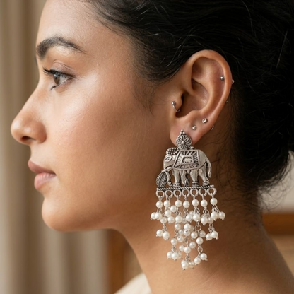 A woman models a single oxidized silver elephant earring with white pearl drops on her right ear.