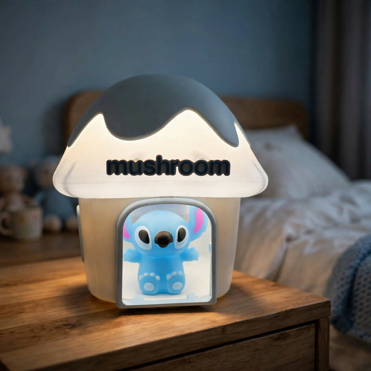 A mushroom house night light with a dark gray cap, illuminating a blue Stitch character on a wooden bedside table.