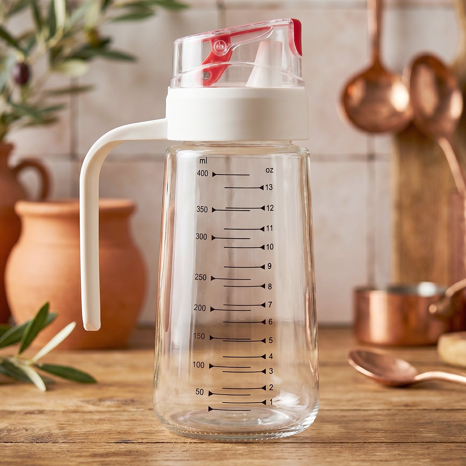 Glass Oil Dispenser Bottle 500ml with Auto-Flip Red Cap, White Side Handle and ml/oz Measurement Scale on Kitchen Counter