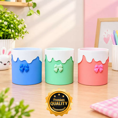 Three empty pastel-colored cylindrical organizers with white wavy tops and small bows on the front.