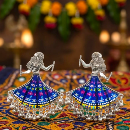 Pair of oxidized silver dancing doll earrings with blue floral skirts on a colorful patterned fabric.